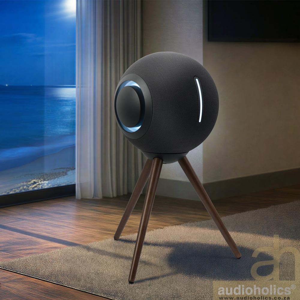 Muse-M-990BT-Main - Audioholics South Africa Black spherical smart speaker on three wooden legs in a modern living room by a large window with beach/ocean view; subtle vertical LED stripe on the sphere's side.