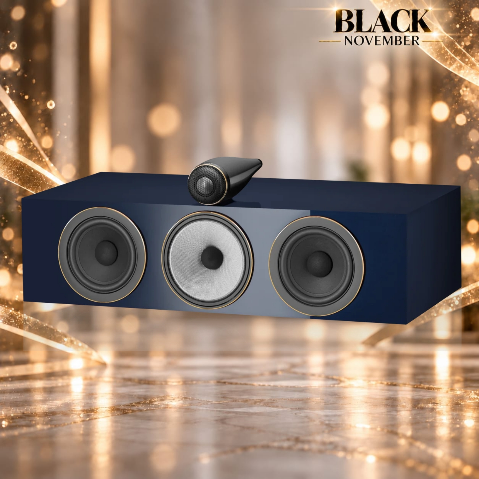 HTM71 SIG - Audioholics South Africa Speaker on a blue display cabinet with three large woofers, a small handheld speaker perched on top, and a gold-festive background reading 'BLACK NOVEMBER'.